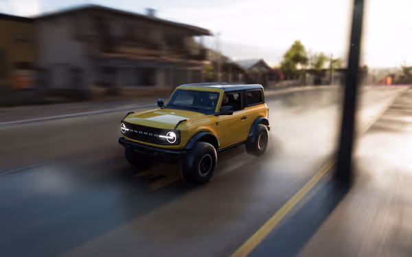 A yellow off-road vehicle driving through a suburban street at speed, with motion blur.