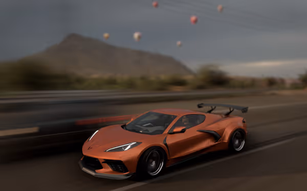 Orange sports car speeding past with balloons and a mountain in the background.