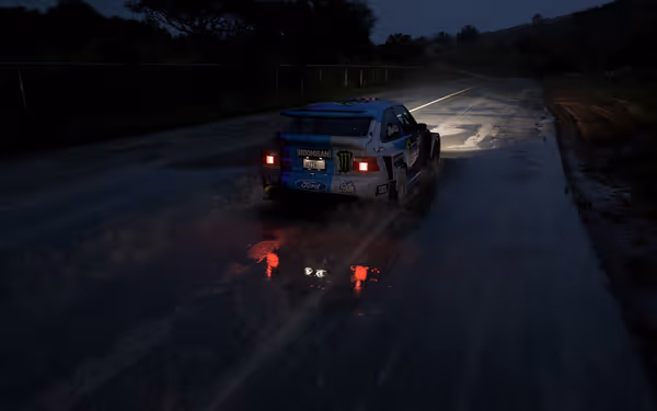  A rally car speeds along a wet road at night, headlights and taillights glowing in the dimly lit surroundings.