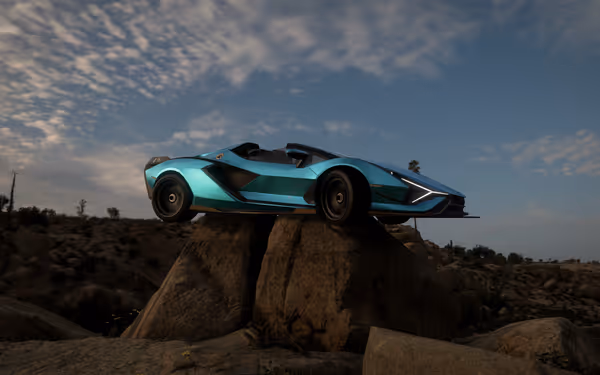 Blue sports car on large rock in desert landscape with cloudy sky.