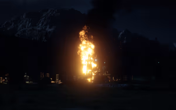 An oil rig is consumed by flames, with smoke billowing into the night sky. A hill looms in the distance.