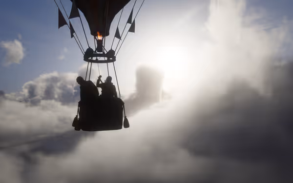 Hot air balloon floating above clouds with silhouettes of people under sunlight.