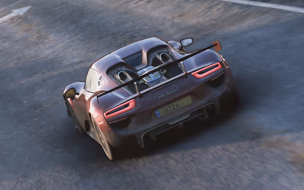 A dusty red sports car driving on a road at a steep left incline