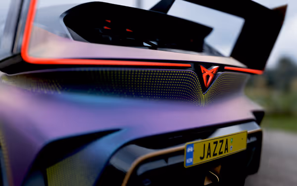 A close up of a polychromatic purple-blue car accented with yellow dots, showing the brake lights on the spoiler and logo, and a numberplate reading "Jazza"