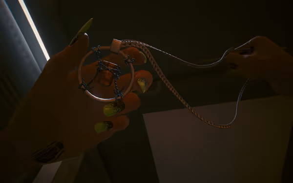 A person with neon green nails holds a metallic necklace with a barbed wire pendant.