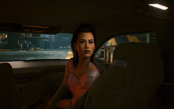A woman with dark hair and bold makeup sits in a futuristic car at night.