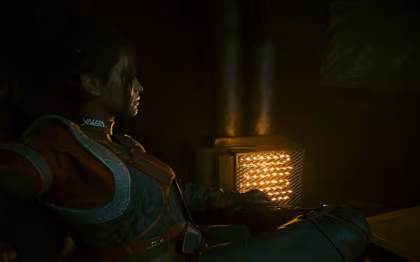A woman in futuristic armor sits near a glowing heater in a dimly lit room.