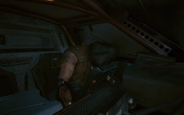 A hooded figure with a bloody arm slumps over inside a rugged armored vehicle.
