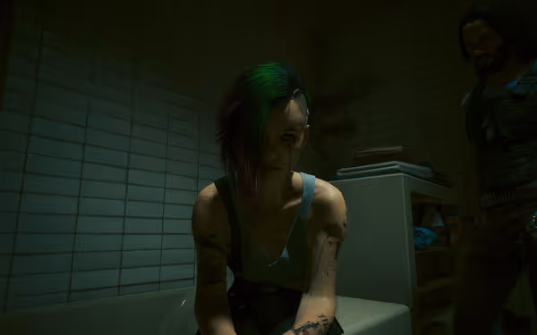 A woman with green-highlighted hair and tattoos sits in a dimly lit bathroom.