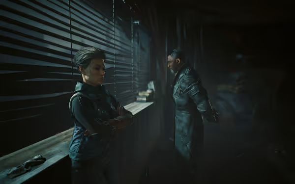 Two serious figures stand in dim light by window blinds, both wearing futuristic gear.