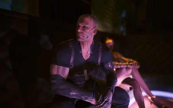 Muscular man with cybernetic implants sits in dim lounge, woman with cyberarms behind.