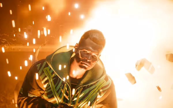 A man in a futuristic jacket stands before an explosion, sparks and debris flying.