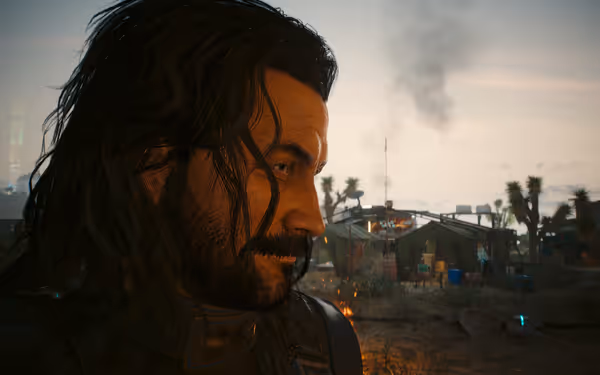 A bearded man with long hair looks down near a desert camp with tents.