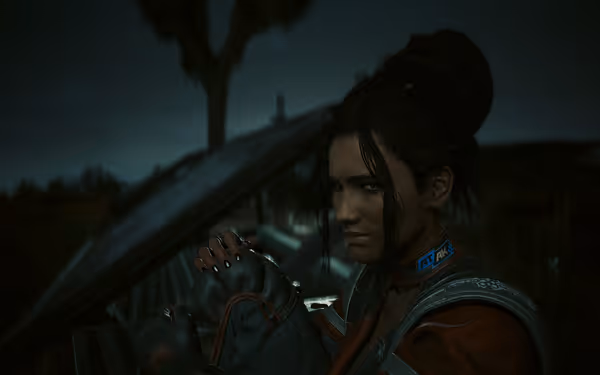 A woman in a futuristic outfit sits in dim light, holding her knee.