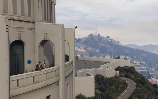 Two men lean over a balcony at an observatory overlooking hills and a landmark sign.