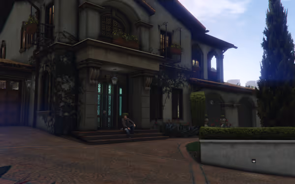 A man sits on the steps of a large, elegant house with ivy-covered walls.