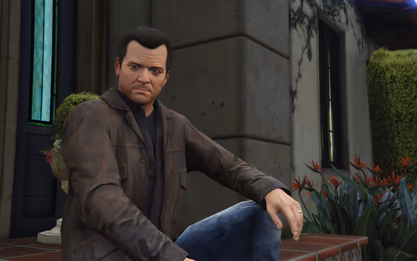 A serious-looking man in a brown jacket sits outside near a flower planter.