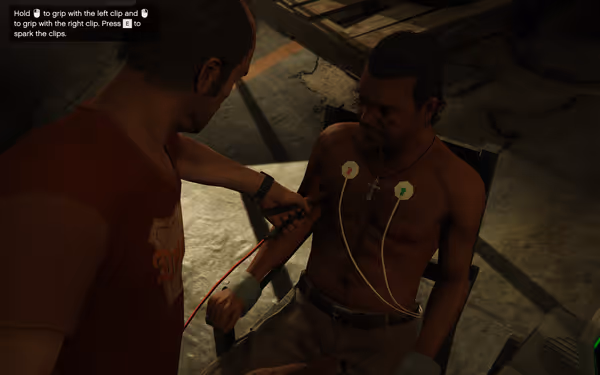 A man in a red shirt holds electric clips near a restrained man.