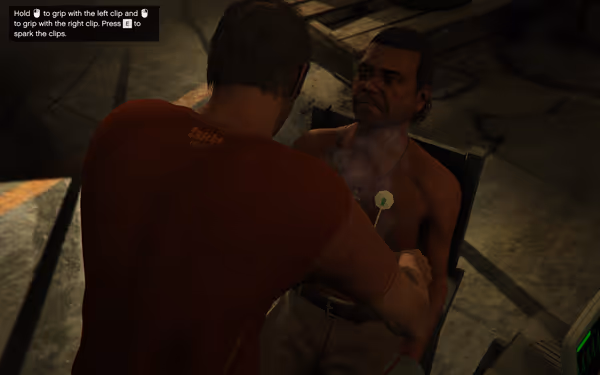 A man in an orange shirt uses electrical clips on a restrained shirtless man.