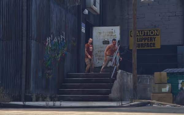 Two men exit a metal building by graffiti and a "Caution Slippery Surface" sign, outside stairs.