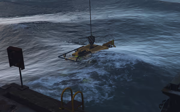 A small yellow submersible is being lowered into rough sea water near a metal dock.