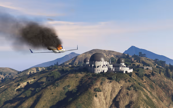 A small jet is on fire mid-air near a large observatory on a hillside.