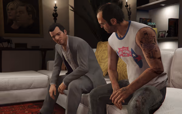 Two men sit on a sofa indoors, one in a suit and one in a tank top.