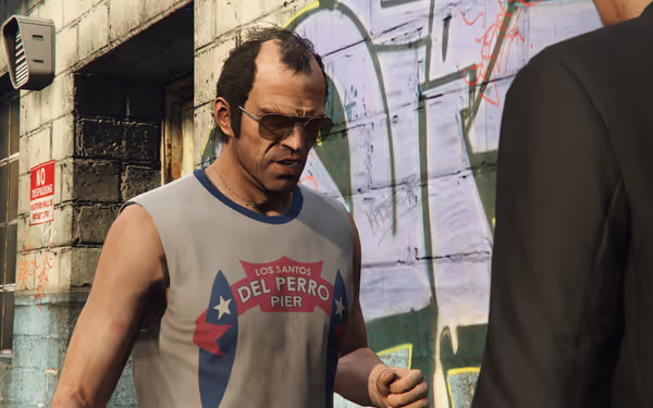 A man in a sleeveless “Del Perro Pier” shirt stands outside beside graffiti wall.