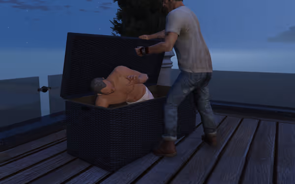 A shirtless man hides in a large black box while another man looks inside.