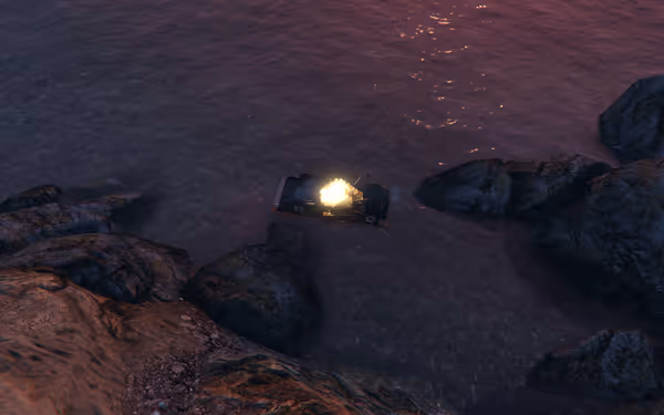 A car in shallow water is on fire, surrounded by rocks and a sandy shore at dusk.