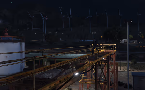 A person walks on a rusted metal walkway at night with wind turbines in the background.