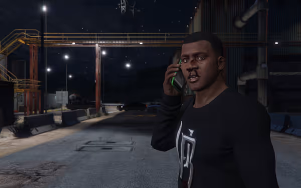 Man in black shirt holding phone to ear stands outside industrial facility at night.