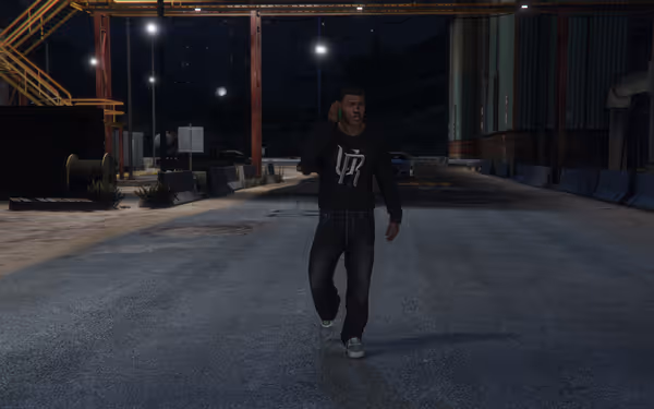 A man in a dark sweatshirt walks on an empty street talking on a cellphone.