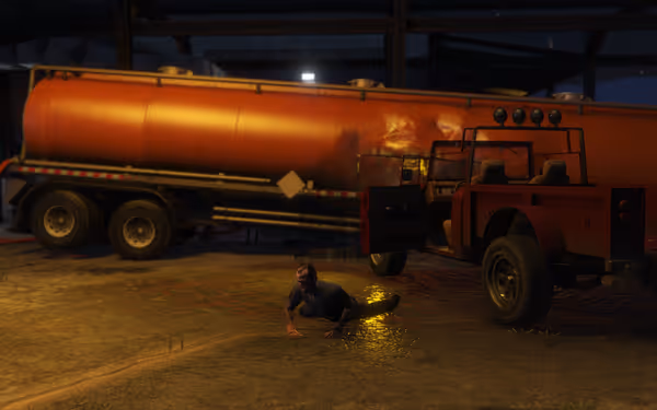 A man is crawling on the ground by a red jeep, with a large orange tanker behind.