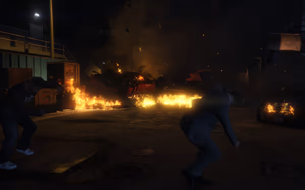 People duck for cover as burning cars and crates fill an area with flames and smoke.