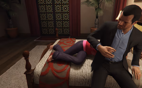 A man in a suit sits on a bed with a woman lying beside him.