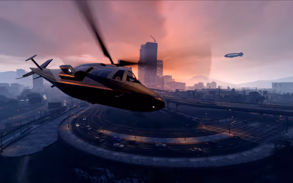 A helicopter flies over a city skyline at sunset, with a blimp in the sky.