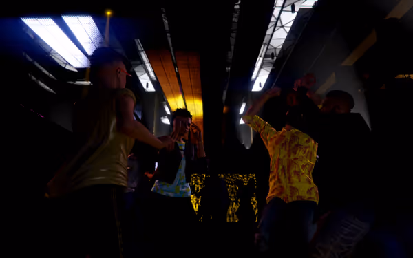 Several people interact in a dark indoor space with industrial ceiling lighting above.